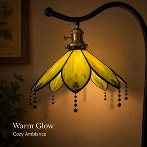 May include: A stained glass lamp shade with yellow, petal-shaped panels and black metal framing. The shade features hanging black beaded accents and a brass-colored socket. The text "Warm Glow Cozy Ambiance" is visible in the lower left corner.