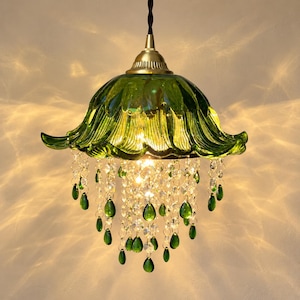 May include: A pendant light fixture featuring a green glass shade shaped like a flower with scalloped edges. The lamp is adorned with numerous clear and green teardrop-shaped glass crystals hanging from the base, suspended by a brass-toned metal cap.