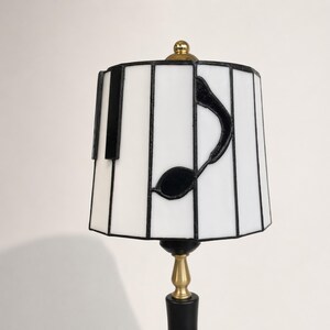 Close-up of the stained glass lampshade showing white glass panels, black solder lines, piano key accents, and music note detail.