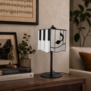 Living room side table with music note stained glass lamp, framed piano art, books, and vintage decor