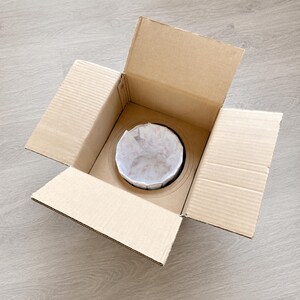 Open cardboard shipping box with custom inner support holding the wrapped piano stained glass table lamp securely for safe delivery.