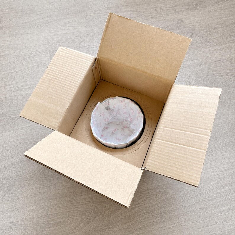 Open cardboard shipping box with custom inner support holding the wrapped piano stained glass table lamp securely for safe delivery.
