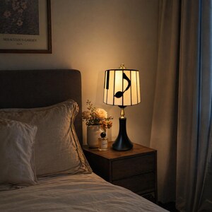Warm piano note table lamp placed on a bedroom nightstand beside a cozy bed, creating soft ambient lighting.