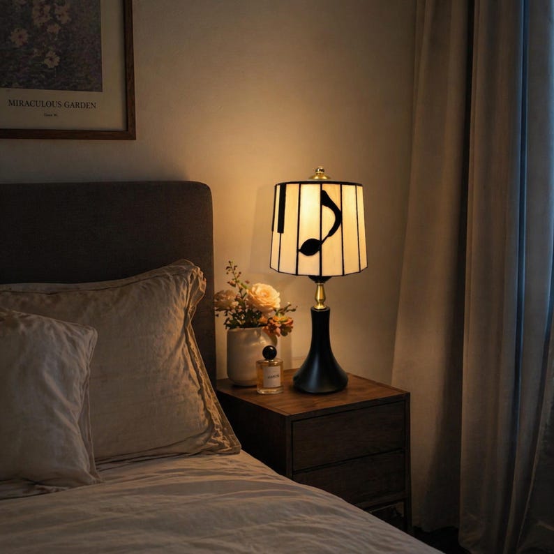 Warm piano note table lamp placed on a bedroom nightstand beside a cozy bed, creating soft ambient lighting.