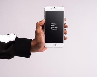 以下が含まれることがあります： 「Think. Plan. Execute. Repeat.」のテキストが表示された黒い画面の白いスマートフォンが手に持たれています。その人は黒と白のスリーブを着ています。背景は無地の明るいグレーです。