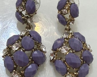 Könnte beinhalten: Ein Paar Ohrhänger mit einer Ansammlung von facettierten, ovalen violetten Steinen und klaren, runden Kristallen in einer goldfarbenen Metallfassung. Jeder Ohrring besteht aus einem kleineren oberen und einem größeren unteren Teil.