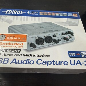Może przedstawiać: Białe kartonowe pudełko na interfejs audio USB Edirol UA-25. Opakowanie zawiera grafikę srebrnego urządzenia audio, napis "USB Audio and MIDI interface" oraz etykietę informującą o dołączonym oprogramowaniu "Cakewalk SONAR LE".