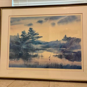 Könnte beinhalten: Ein gerahmtes Aquarellbild, das eine ruhige Landschaft mit einem See, Bäumen und einem einzelnen Vogel zeigt, der im Wasser steht. Der Himmel ist in einem sanften Blau mit zarten Wolken gehalten. Das Bild ist in einem dunklen Holzrahmen mit goldener Verzierung gerahmt.