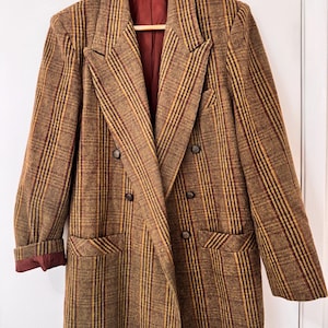 Peut inclure: Un blazer croisé avec un motif à rayures verticales marron, doré et rouge foncé. Le vêtement présente de larges revers, deux poches à rabat sur le devant et des boutons marron foncé. L'intérieur est doublé d'un tissu rouge foncé uni.