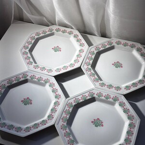 May include: Set of four white octagonal plates with a floral design. Each plate features a border of pink and green floral patterns and a central floral bouquet. The plates are arranged on a white surface.