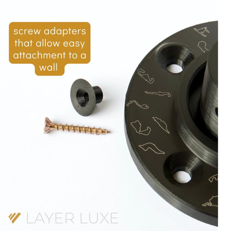 May include: A black wall mount with a screw adapter and a screw. The wall mount has a circular design with a raised edge and a hole in the center. The screw adapter is a small, black plastic piece with a hole in the center. The screw is a small, brown metal piece with a pointed end.