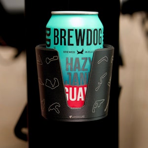 May include: A blue and white can of Brewdog Hazy Jane Guava beer in a black cup holder with a white racing track design. The text "Brewdog" is in black and the text "Hazy Jane Guava" is in red and white.