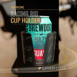 Puede incluir: Portavasos negro con contornos blancos de pistas de carreras, que sostiene una lata de cerveza Brewdog. La lata es de color turquesa con las palabras "Hazy Jane" y "Brewed in Ello". El texto "Racing Rig Cup Holder" está en la parte superior.