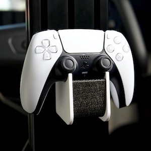 May include: A white PlayStation 5 DualSense controller with black buttons and a black and white patterned stand. The controller is mounted on the stand.