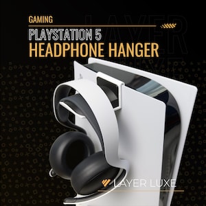 May include: White PlayStation 5 headphone hanger with a black and white headset. The hanger is designed to hold headphones and is mounted on the side of the console. The image includes the text "GAMING PLAYSTATION 5 HEADPHONE HANGER" and "LAYER LUXE".