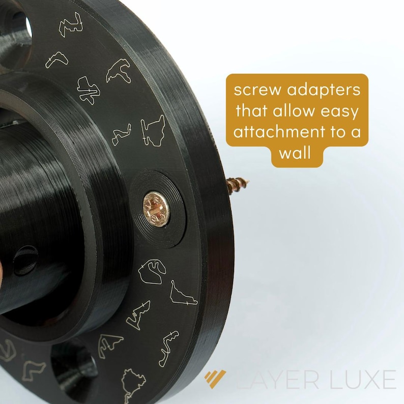 May include: Close-up of a black metal wall mount with screw adapters. The mount has a circular design with a textured surface and a small screw hole in the center. The text "screw adapters that allow easy attachment to a wall" is visible in the image.