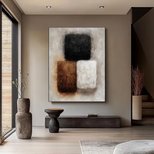 May include: Abstract wall art featuring a composition of three textured squares in black, brown, and white against a neutral background. The artwork is framed and displayed in a modern interior setting.