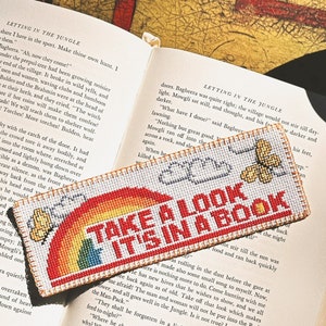 May include: A white bookmark with a rainbow and clouds design. The bookmark has the text "Take a look it's in a book" in red letters.