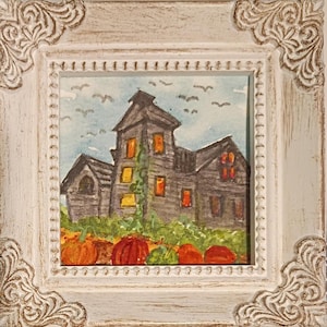 May include: A framed watercolor painting depicting a dark, multi-story house with glowing orange windows, surrounded by a patch of orange pumpkins and green foliage under a light blue sky with small birds flying in the distance.
