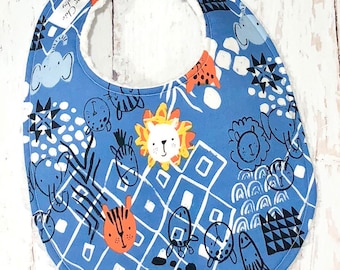 Pode incluir: Babador azul para bebé com forro polar branco nas costas. O babador apresenta uma estampa colorida de animais, incluindo leões, tigres, zebras e elefantes. O texto "Sweet Chic Baby" está impresso no babador.