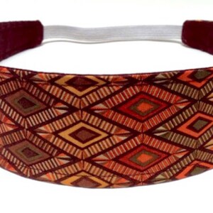 May include: A wide headband with an elastic back. The headband features a geometric pattern in shades of orange, brown, and gold. The interior is a solid burgundy color.