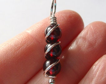 May include: A silver wire wrapped pendant with four dark red garnet beads.