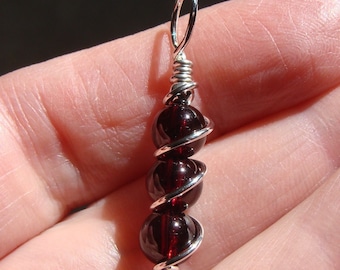 May include: A silver wire-wrapped pendant with four dark red garnet beads.
