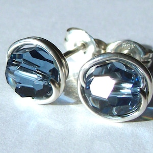 May include: A pair of stud earrings featuring faceted, dark blue crystals set in a silver wire frame. The earrings have a post backing for pierced ears. The crystals reflect light, creating a sparkling effect. Jewelry.