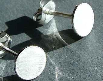 May include: A pair of silver stud earrings with a round, brushed metal design. The earrings are simple and elegant.