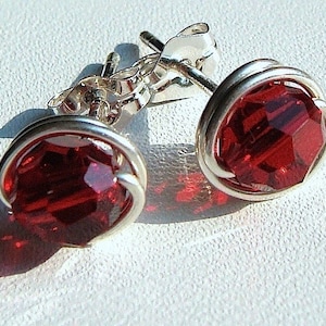 May include: A pair of silver earrings with red crystal stones. The earrings are made with wire wrapped around the stones.