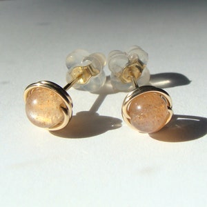 May include: A pair of gold earrings with a sunstone gemstone in each. The earrings are set in a simple wire design.