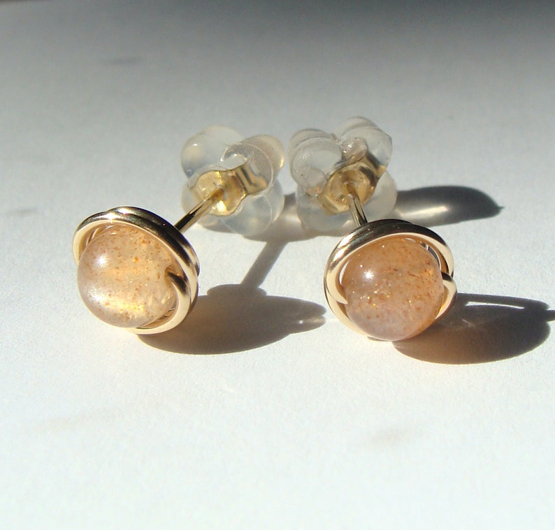 May include: A pair of gold earrings with a sunstone gemstone in each. The earrings are set in a simple wire design.