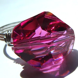 May include: A silver ring with a large, faceted, pink crystal. The crystal is shaped like a square with rounded edges.