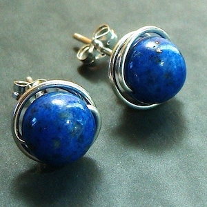May include: A pair of silver earrings featuring blue lapis lazuli stones. The stones are set in a wire cage design.