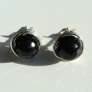 May include: A pair of silver earrings with black gemstone accents. The gemstones are round and have a faceted finish.