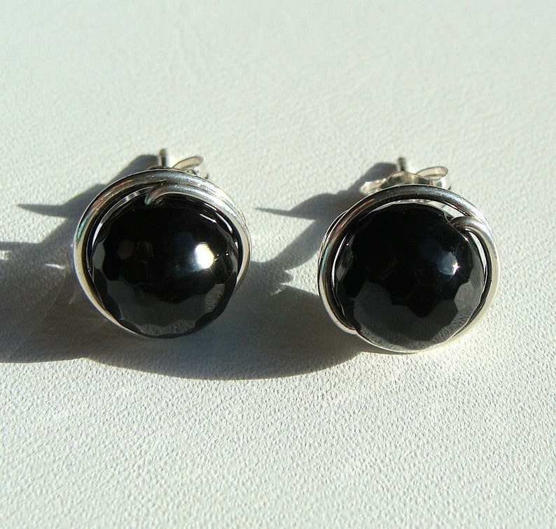 May include: A pair of silver earrings with black gemstone accents. The gemstones are round and have a faceted finish.