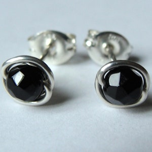 May include: A pair of stud earrings featuring faceted black gemstones set in a silver metal. The gemstones are round and surrounded by a twisted silver wire design. The earring backs are also visible.