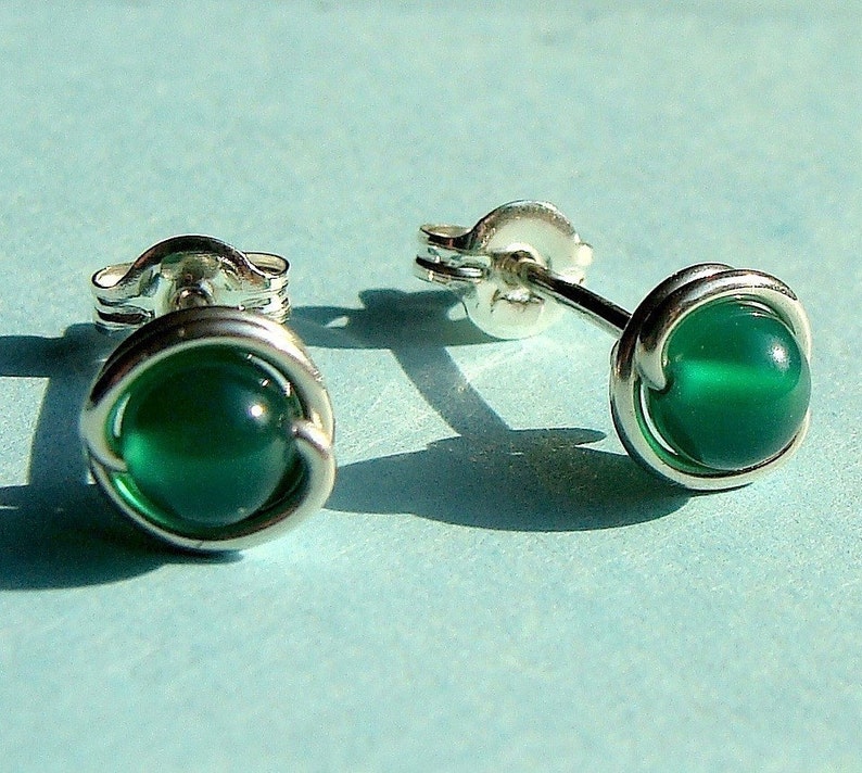 Peut inclure: Une paire de boucles d'oreilles en argent avec des accents de pierres pr&eacute;cieuses vertes. Les boucles d'oreilles sont faites avec un design en fil de fer.