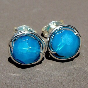 May include: A pair of silver earrings with a turquoise blue gemstone in each. The gemstones are faceted and have a wire cage around them.