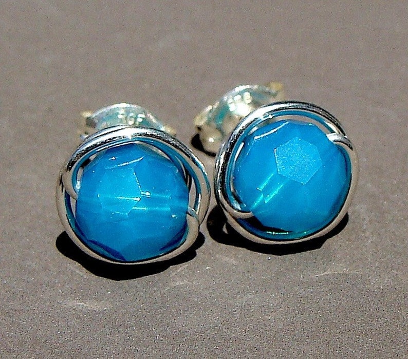 May include: A pair of silver earrings with a turquoise blue gemstone in each. The gemstones are faceted and have a wire cage around them.