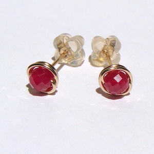 Peut inclure: Une paire de boucles d'oreilles à clous avec des pierres précieuses rouge foncé facettées, serties dans du fil de couleur or. Les boucles d'oreilles ont une tige et un fermoir pour un port sûr. Les pierres précieuses sont rondes et captent la lumière.