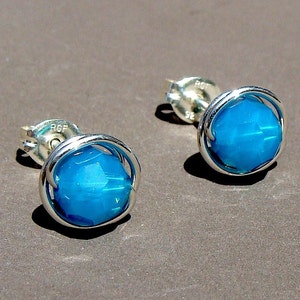 May include: A pair of silver stud earrings with a turquoise blue gemstone in each. The gemstones are surrounded by a silver wire frame.