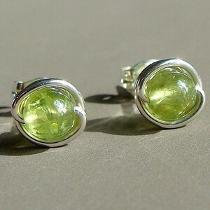 May include: A pair of silver earrings with green gemstone accents. The earrings are made of wire that is wrapped around the gemstones.