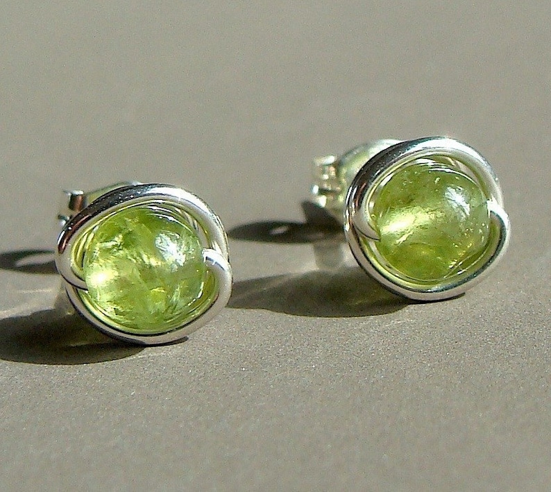 May include: A pair of silver earrings with green gemstone accents. The earrings are made of wire that is wrapped around the gemstones.