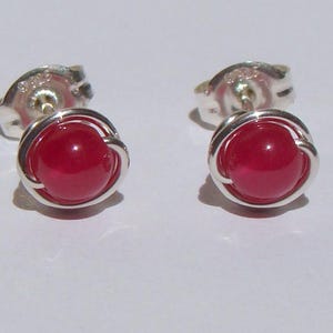 May include: A pair of stud earrings featuring a vibrant red, round gemstone set in a silver-colored metal. The earrings have a post and backing for secure wear. The gemstones are approximately 0.25 inches in diameter.