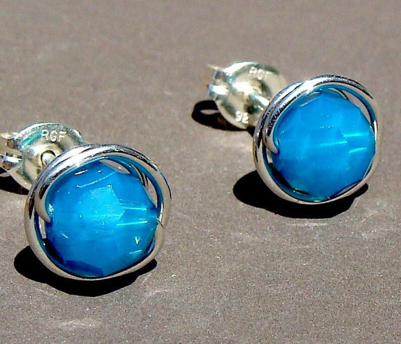 May include: A pair of silver stud earrings with a blue gemstone set in a silver wire cage.