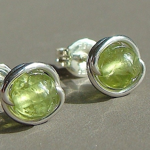 May include: A pair of silver earrings with green peridot gemstones. The gemstones are set in a simple wire design.