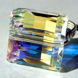 May include: A ring with a large, faceted, iridescent crystal set in a silver wire wrap. The crystal is a rectangular shape with a yellow, blue, and purple color scheme.