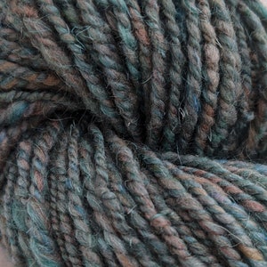 May include: Close-up of a skein of thick, textured yarn. The yarn is a blend of teal, brown, and blue hues, with a slightly fuzzy texture. The strands are tightly twisted, creating a chunky appearance, ideal for knitting or crocheting projects.