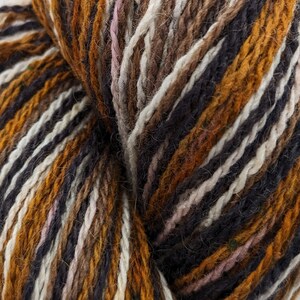 May include: Close-up of a skein of yarn with brown, white, black, and orange stripes. The yarn is soft and fluffy, and the colors are vibrant.